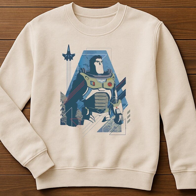 May include: A cream-colored crewneck sweatshirt featuring a graphic print of a stylized space ranger character in a white, blue, and green suit. The design includes geometric shapes, thin lines, and a small aircraft silhouette in the background.