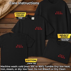 K&ouml;nnte beinhalten: Eine Kollektion schwarzer Kleidungsst&uuml;cke, bestehend aus einem kurz&auml;rmeligen T-Shirt und einem lang&auml;rmeligen Pullover mit Rundhalsausschnitt, jeweils mit dem roten Schriftzug "HAIL HYDRA" auf der Brust. Pflegehinweise: Maschinenw&auml;sche bei 30C, trocknergeeignet.