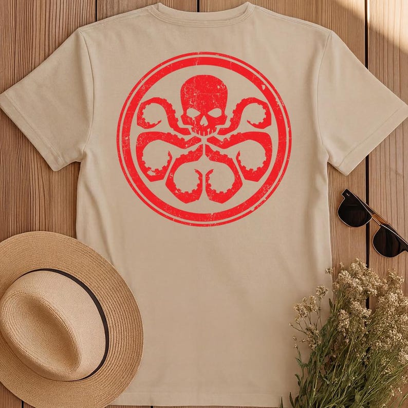 K&ouml;nnte beinhalten: Ein beiges Kurzarm-T-Shirt mit einer gro&szlig;en, kreisf&ouml;rmigen roten Grafik auf der R&uuml;ckseite. Das Design zeigt einen verwitterten Totenkopf in einem Kreis, der von mehreren tentakelartigen Armen umgeben ist, die nach au&szlig;en ragen.