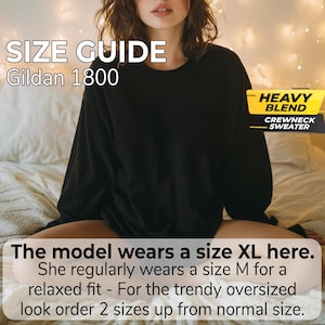 May include: A black crewneck sweater with long sleeves. Text on the image reads: SIZE GUIDE Gildan 1800, HEAVY BLEND CREWNECK SWEATER, The model wears a size XL here. She regularly wears a size M for a relaxed fit - For the trendy oversized look order 2 sizes up from normal size.