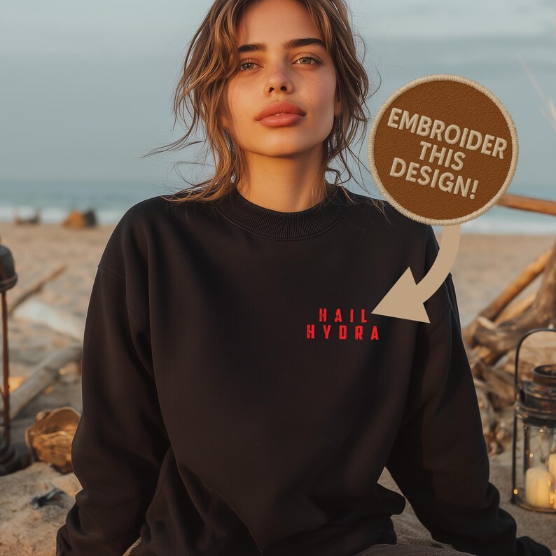 K&ouml;nnte beinhalten: Ein schwarzes Sweatshirt mit Rundhalsausschnitt und dem roten Schriftzug "HAIL HYDRA" auf der linken Brust. Ein runder brauner Aufn&auml;her mit dem wei&szlig;en Text "EMBROIDER THIS DESIGN!" ist durch einen beigen Pfeil mit dem Text verbunden.