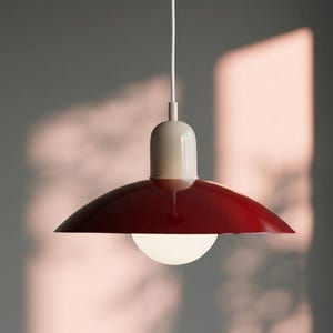 Peut inclure: Une suspension moderne avec un abat-jour rouge foncé et un dessus crème. La lampe a une ampoule sphérique blanche et un cordon blanc. Le design est minimaliste et convient à divers styles d'intérieur.