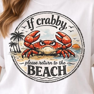 May include: White t-shirt featuring a circular graphic with a crab illustration. The crab is red with an angry expression, set against a beach scene with palm trees and a sunset. Text reads "If crabby, please return to the BEACH."