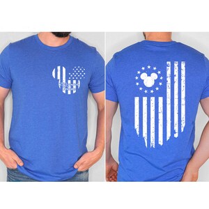 May include: Blue t-shirt featuring a white Mickey Mouse-shaped design with a stars and stripes pattern and the text "250 Years of Freedom" on the front. The back of the shirt displays a distressed American flag design.