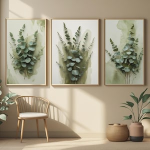 Peut inclure: Trois impressions botaniques encadrées représentant des feuilles d'eucalyptus à l'aquarelle dans des tons de vert et de gris. Les impressions ont un fond beige clair et sont exposées dans une pièce avec une chaise en bois, un panier tressé et une plante en pot.