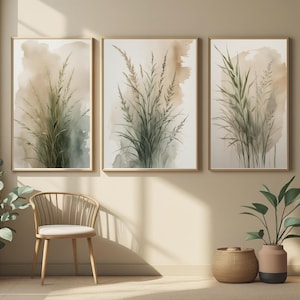 Peut inclure: Trois impressions encadrées à l'aquarelle représentant de hautes herbes vertes sur un fond doux et neutre. L'œuvre d'art a un thème botanique naturel, avec un cadre en bois brun clair. Les impressions sont affichées au-dessus d'une chaise et d'objets décoratifs.