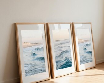 Peut inclure: Trois tirages encadrés représentant des vagues océaniques. Les photographies montrent des vagues bleues et blanches avec une plage de sable et le ciel. Les cadres sont en bois clair. Les tirages sont appuyés contre un mur.