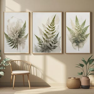 Peut inclure: Trois impressions encadrées à l'aquarelle représentant des frondes de fougères dans des tons verts et gris. L'œuvre d'art a une qualité douce et éthérée, les fougères se détachant sur un fond clair. Les cadres sont en bois naturel et chaleureux.