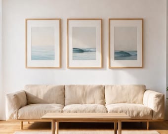Peut inclure: Un salon moderne avec un canapé beige, une table basse en bois et trois tableaux encadrés représentant des vagues océaniques. La pièce est dotée d'un parquet et d'un tapis neutre, créant une atmosphère minimaliste et apaisante.