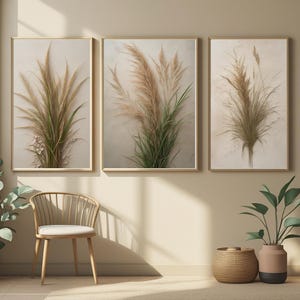 May include: Three framed botanical prints featuring dried pampas grass in shades of beige, brown, and green. The artwork is displayed on a light beige wall, creating a neutral and natural aesthetic. The frames are a light wood color.