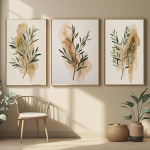 Peut inclure: Trois impressions d'art botanique encadrées. Chaque impression présente une illustration à l'aquarelle de branches d'olivier avec des feuilles vertes et un fond marron et beige. Les cadres sont de couleur bois clair, et l'esthétique générale est minimaliste et naturelle.
