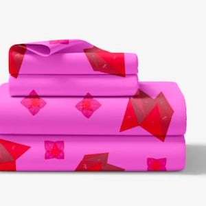 May include: A stack of pink bed sheets with a geometric pattern in red and maroon. The sheets are folded neatly, showcasing the design. The pattern includes diamond and triangular shapes.