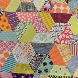 May include: Close-up of a colorful patchwork quilt with a geometric design. The quilt is composed of various hexagonal fabric pieces in a variety of patterns and colors, including polka dots, stripes, and floral prints.