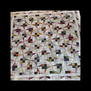 May include: A handmade quilt with a repeating starburst pattern. The quilt features a neutral background with colorful starbursts in shades of red, orange, green, and purple. The starbursts are interspersed with black squares.