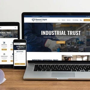 May include: A laptop, tablet, and smartphone showing a website with the words "INDUSTRIAL TRUST." A yellow hard hat and a coffee mug are placed nearby. A rolled-up blueprint is on the wooden surface.