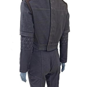 May include: Dark gray jumpsuit with brown shoulder accents and white stitching. The sleeves have geometric patterns near the elbow. The back of the jumpsuit has a vertical seam and horizontal stitching across the shoulders and waist.