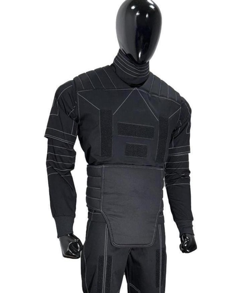 Puede incluir: Un conjunto t&aacute;ctico negro de camisa de manga larga y pantal&oacute;n con cuello alto, paneles acolchados en los hombros y una secci&oacute;n abdominal reforzada. La prenda incluye costuras blancas en contraste y m&uacute;ltiples parches rectangulares de velcro.