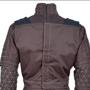 May include: A dark brown jacket featuring a high collar with a zipper closure, white contrast stitching, and black padded shoulder details. The sleeves display a geometric quilted pattern, while the back panel includes a vertical central seam.