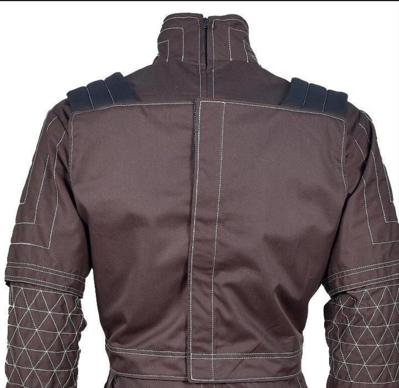 May include: A dark brown jacket featuring a high collar with a zipper closure, white contrast stitching, and black padded shoulder details. The sleeves display a geometric quilted pattern, while the back panel includes a vertical central seam.