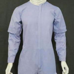 Puede incluir: Un mono de color azul claro con un cuello alto blanco acanalado, mangas largas con una capa adicional de manga corta en los hombros y dos grandes bolsillos de parche en la parte delantera de los muslos, expuesto sobre un maniqu&iacute; blanco.