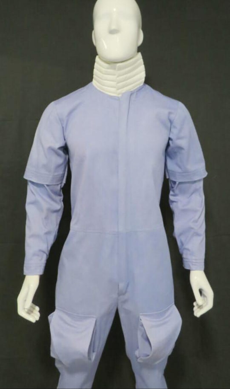 Puede incluir: Un mono de color azul claro con un cuello alto blanco acanalado, mangas largas con una capa adicional de manga corta en los hombros y dos grandes bolsillos de parche en la parte delantera de los muslos, expuesto sobre un maniqu&iacute; blanco.