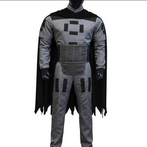 May include: A gray long-sleeved jumpsuit featuring a black high collar, a black cape with a jagged hem, and a wide black waist belt. The garment is decorated with black rectangular patches on the chest and thighs, and includes black wrist cuffs.