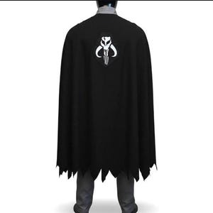 May include: A black cape featuring a white Mythosaur skull emblem centered on the upper back. The cape has a jagged, uneven hemline at the bottom and is worn over a grey collared shirt and grey trousers, covering the back of the torso.