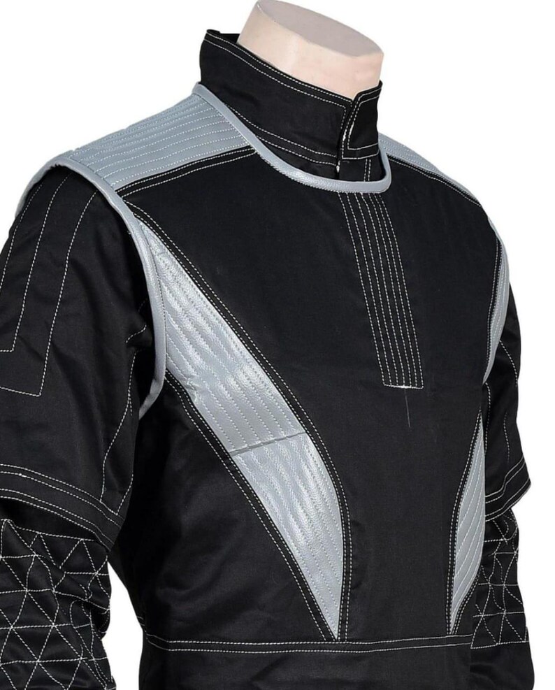 May include: Black jacket with silver accents and white stitching. The jacket features a high collar and quilted shoulder and chest panels. The design includes geometric patterns on the sleeves, creating a futuristic aesthetic.