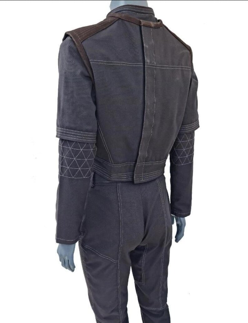 May include: A dark charcoal gray jacket and matching trousers set featuring a high collar, structured shoulders, and white contrast stitching. The jacket sleeves have a distinct geometric quilted pattern on the forearms and a cropped hemline.