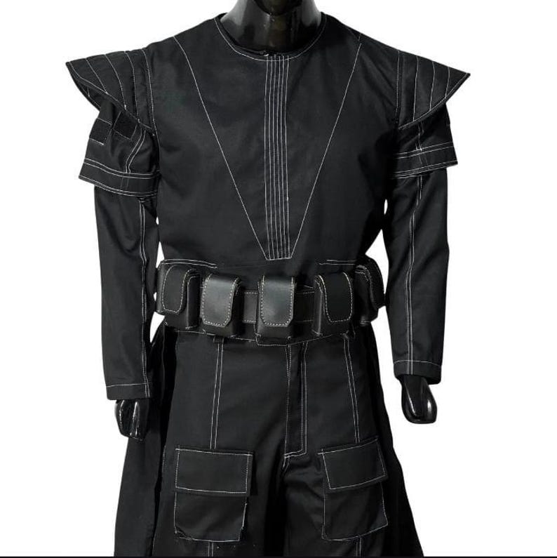 May include: Black costume with white stitching. The outfit has a high collar, structured shoulders, long sleeves, and a belt with pouches. The trousers have large pockets. The costume is displayed on a mannequin.