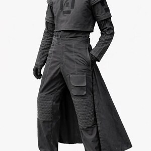 K&ouml;nnte beinhalten: Ein dunkelgraues futuristisches Outfit. Das Ensemble umfasst ein kurzes Oberteil mit geometrischem Design, eine lang&auml;rmlige Unterschicht, eine hoch taillierte Hose mit Knieschonern und einen langen, flie&szlig;enden Rock. Das Outfit wird durch Handschuhe und Schuhe erg&auml;nzt.