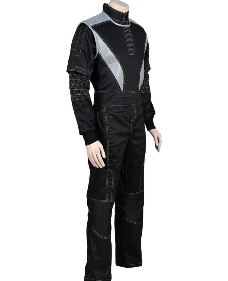 May include: Black racing suit with silver accents and white stitching. The suit features a high collar, a zip-up front, and reinforced panels on the knees. The sleeves have a unique geometric design. The suit is displayed on a mannequin.