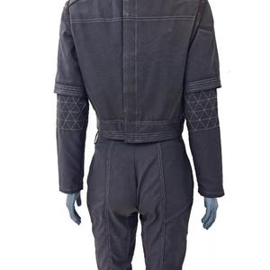 May include: A dark gray jacket and matching trousers set featuring a high collar, long sleeves with quilted diamond-patterned elbow patches, and prominent white topstitching throughout the garment. The jacket has a cropped length and the trousers are fitted.