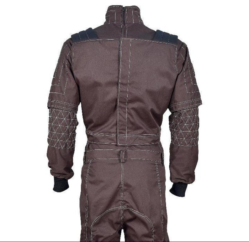 May include: A dark brown jumpsuit featuring a high collar with a zipper closure, long sleeves with quilted triangular patterns on the forearms, black ribbed cuffs, and prominent white contrast stitching throughout the garment's seams and panels.
