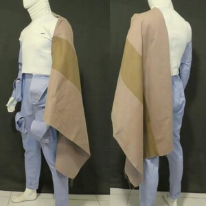 Puede incluir: Un top de cuello alto blanco combinado con pantalones cargo azul claro con m&uacute;ltiples bolsillos. Una pieza de tela drapeada de dos tonos en tonos bronceado y malva cuelga sobre un hombro, extendi&eacute;ndose por el costado del conjunto en un maniqu&iacute;.