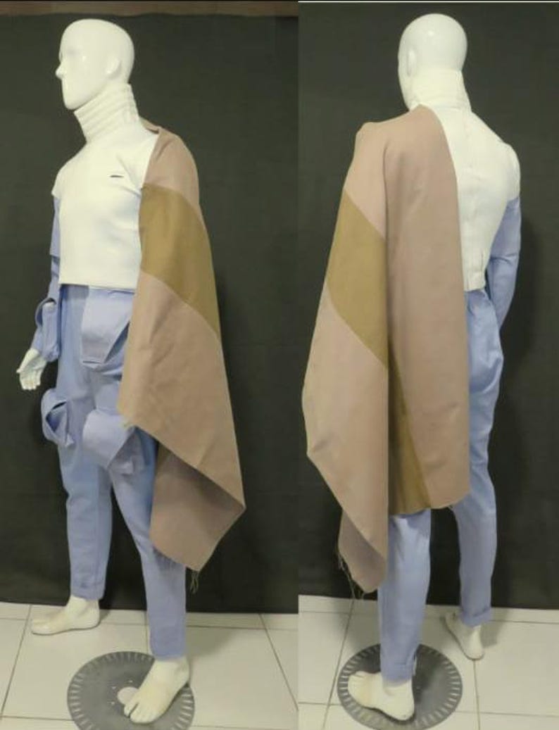 Puede incluir: Un top de cuello alto blanco combinado con pantalones cargo azul claro con m&uacute;ltiples bolsillos. Una pieza de tela drapeada de dos tonos en tonos bronceado y malva cuelga sobre un hombro, extendi&eacute;ndose por el costado del conjunto en un maniqu&iacute;.