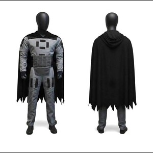 May include: A costume set consisting of a gray long-sleeved top and matching pants featuring black rectangular accents on the chest, shoulders, and thighs. A black hooded cape with a jagged hemline is worn over the outfit, which is displayed on a mannequin.
