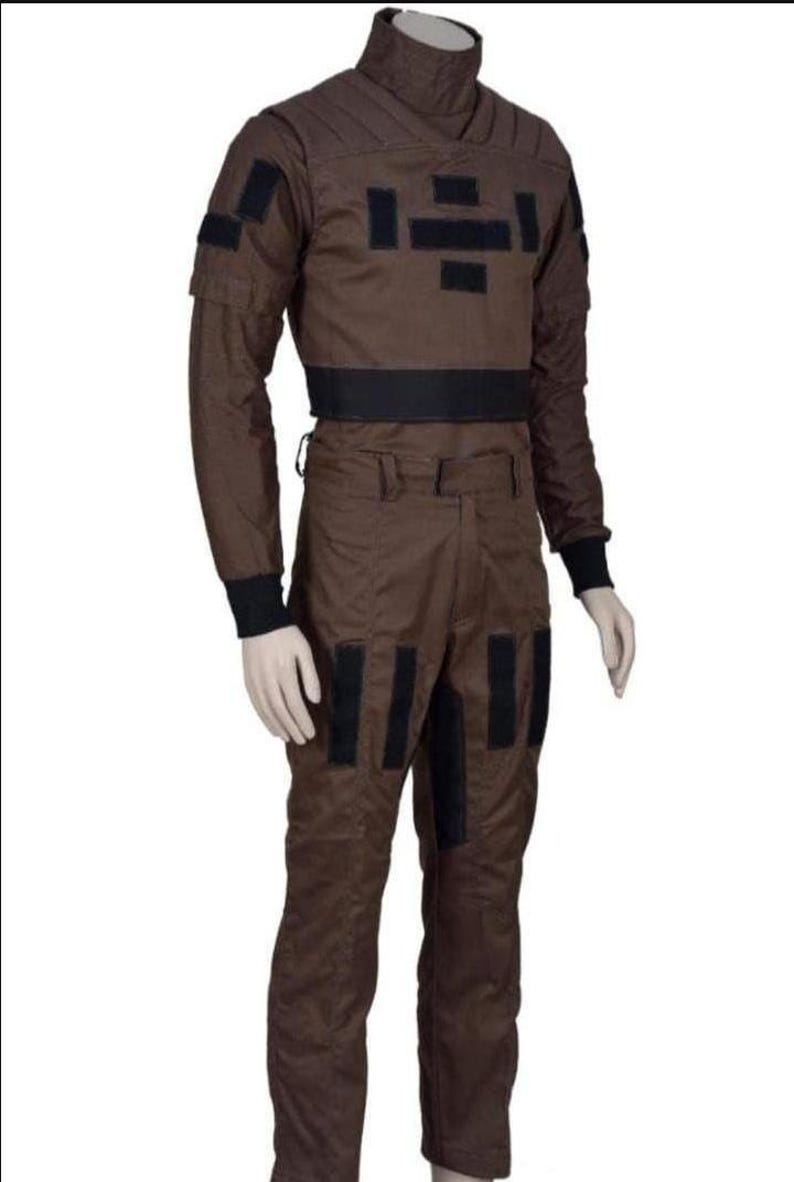 May include: Brown jumpsuit with black accents. The outfit features a high collar, long sleeves, and multiple black rectangular patches on the chest, arms, and legs. A black band defines the waist. The jumpsuit is designed for a costume or cosplay.