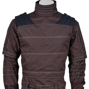 May include: A dark brown long-sleeve shirt featuring a high mock neck collar, horizontal white topstitching, and dark navy blue shoulder panels. The garment includes structured sleeve detailing with multiple rows of white stitching across the arms.