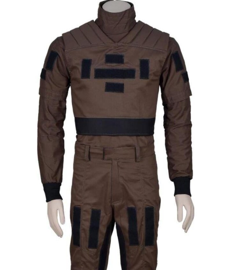 May include: Brown jumpsuit with black accents. The outfit features a high collar, padded shoulders, and multiple rectangular patches. Black bands are on the waist and lower legs. The sleeves have black cuffs.