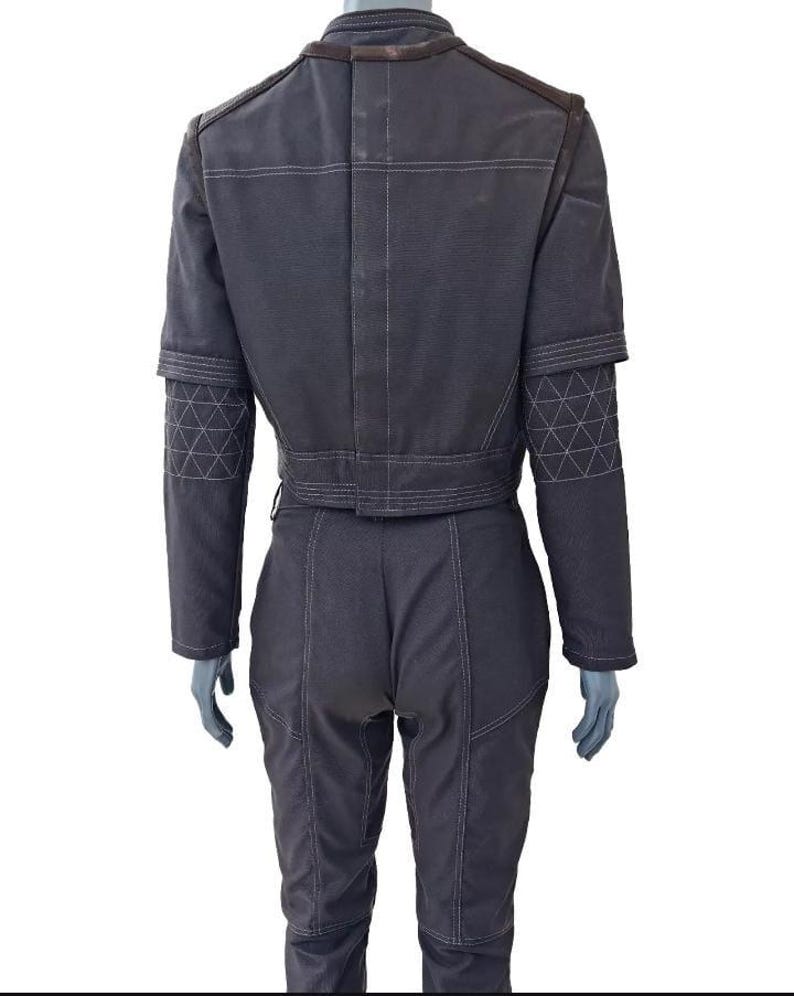 May include: Dark gray jumpsuit with white stitching details. The jacket has a cropped design with a belt, and the sleeves feature geometric patterns. The shoulders and collar have brown accents. The pants are fitted with visible seams.