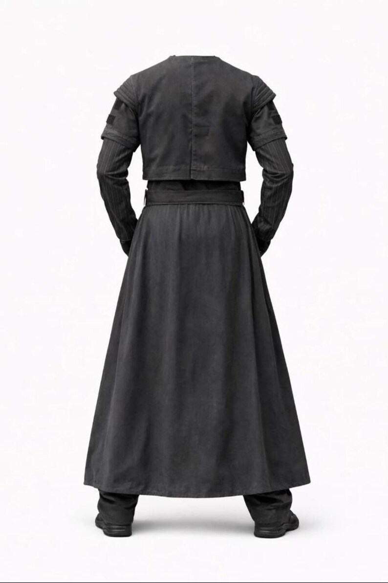 K&ouml;nnte beinhalten: Ein schwarzes Outfit bestehend aus einer cropped Jacke mit Schulterdetails, einem langen Rock und einer Hose. Die Jacke hat lange &Auml;rmel mit einem dezenten Streifenmuster. Der Rock ist weit und flie&szlig;end, und die Hose ist gerade geschnitten.