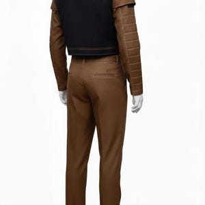 Puede incluir: Un conjunto de dos piezas marr&oacute;n y negro. La chaqueta es negra con detalles marrones y hombros acolchados. Los pantalones son de color marr&oacute;n liso. El conjunto se muestra en un maniqu&iacute;.