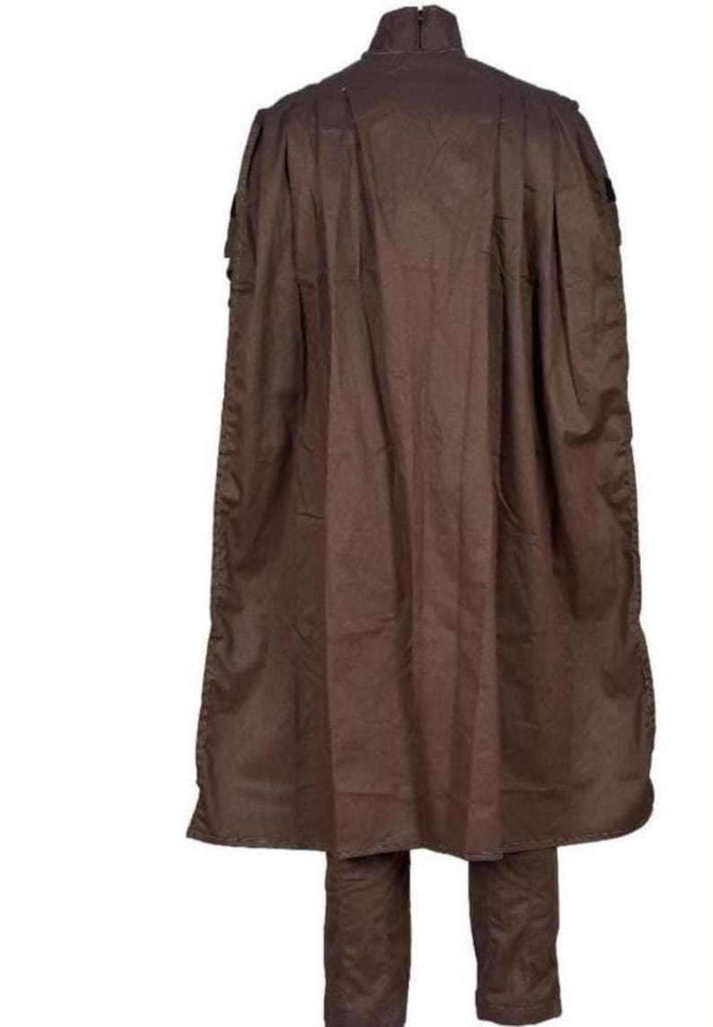 May include: A brown costume consisting of a long cape and matching pants. The cape has a high collar and is pleated at the shoulders. The pants are straight-legged and the fabric appears to be a lightweight material.