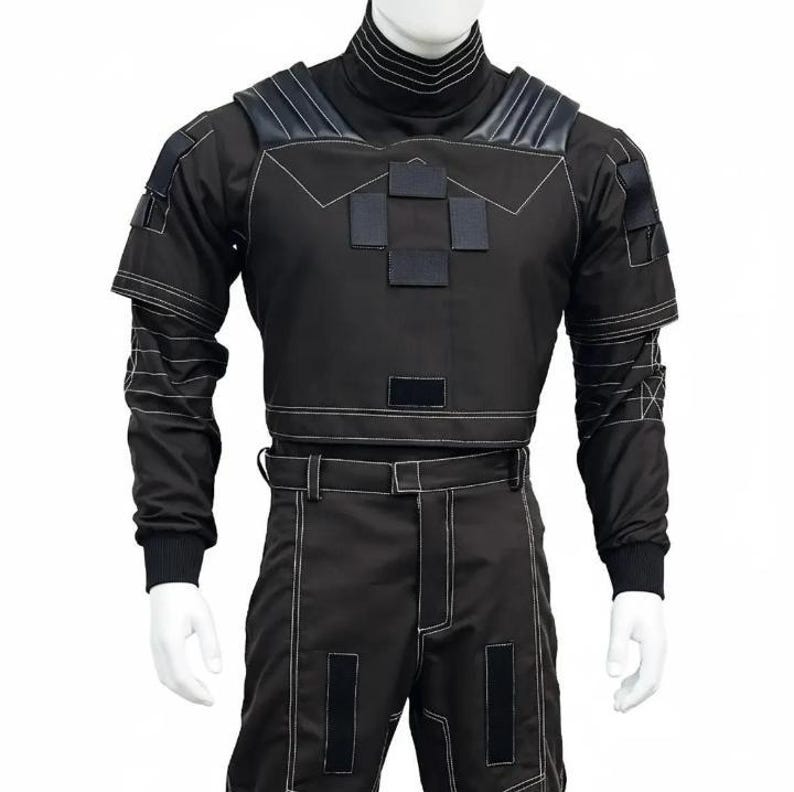 May include: Black tactical outfit with white stitching details. The outfit includes a high-neck top with shoulder accents and a cropped waist, paired with matching pants. The design features multiple square patches and a belt.