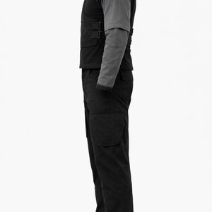Puede incluir: Un atuendo t&aacute;ctico negro, que incluye un chaleco, una camisa de manga larga y pantalones cargo. El chaleco tiene m&uacute;ltiples correas y hebillas. La camisa de manga larga es gris. Los pantalones cargo tienen bolsillos grandes en las piernas.