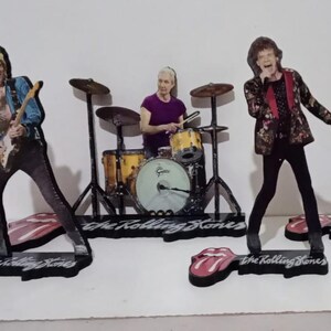 Könnte beinhalten: Eine Sammlung von Figuren der Bandmitglieder der Rolling Stones. Jede Figur ist ein Ausschnitt mit einem Sockel mit der Aufschrift "The Rolling Stones". Die Bandmitglieder spielen Instrumente, darunter Gitarren und Schlagzeug. Die Figuren stehen auf einer weißen Oberfläche.