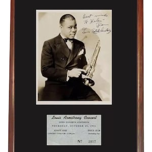 Può includere: Fotografia in bianco e nero incorniciata di Louis Armstrong con tromba, firma e biglietto del concerto del 1951. La cornice è marrone con un passe-partout nero.