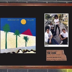Op de afbeelding: Ingelijst kunstwerk met The Cure. Het bevat de albumhoes van "Boys Don't Cry", een bandfoto en een concertkaartje. De lijst is bruin. De albumhoes heeft palmbomen.