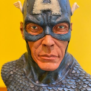 Puede incluir: Busto detallado de Capit&aacute;n Am&eacute;rica, con un casco azul con una "A" blanca y detalles alados. El busto muestra la m&aacute;scara del personaje, sus rasgos faciales y un dise&ntilde;o de armadura texturizada en forma de escamas. La paleta de colores incluye tonos de azul, rojo y blanco.